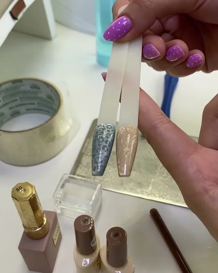 As 2 unhas prontas no mostruário, uma cinza e uma nude, com a oncinha.