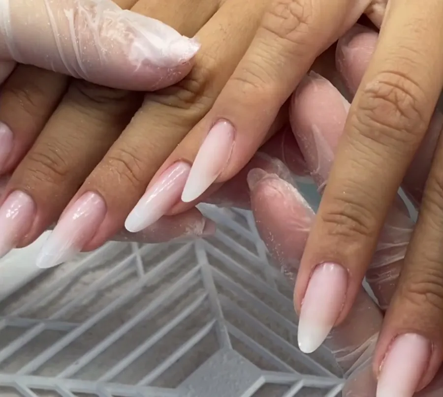 As duas mãos da cliente cruzadas, com as unhas almond prontas, para comparar dedo a dedo.