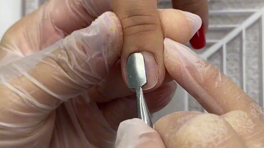 A espátula afastando a cutícula da unha natural.